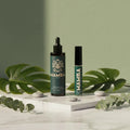 Two Mamba oil bottles on a white surface with green leaves and stones.