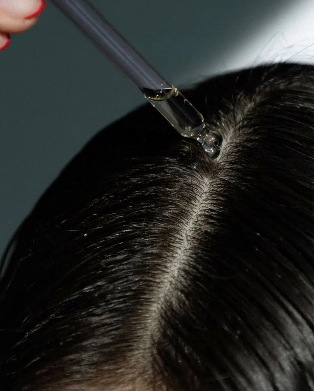 Person applying a clear liquid to hair with a dropper.
