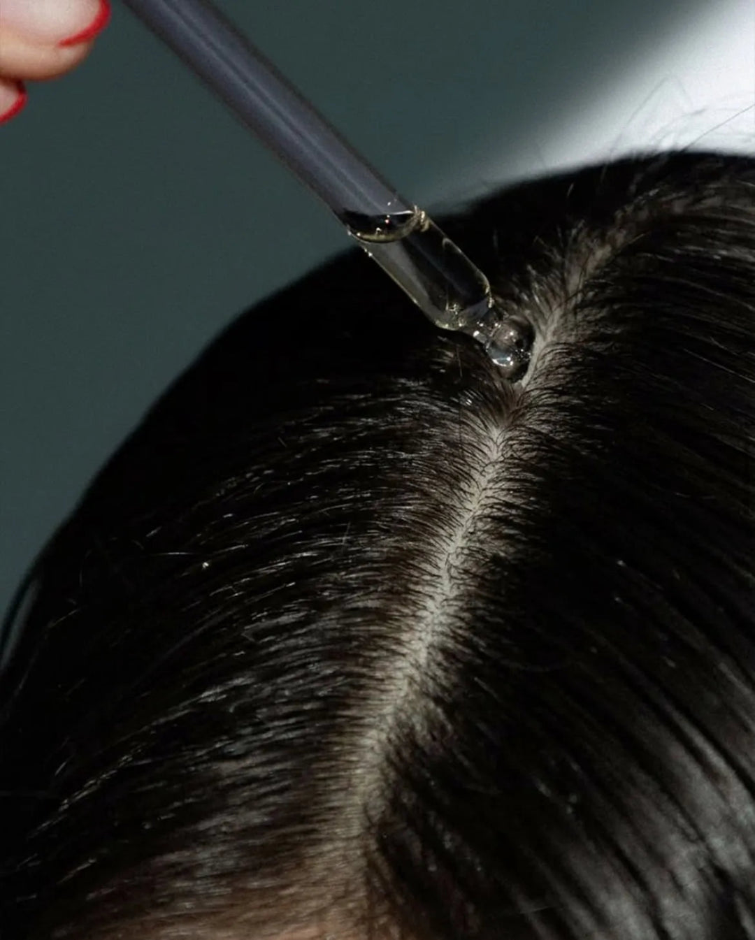 Person applying a clear liquid to hair with a dropper.